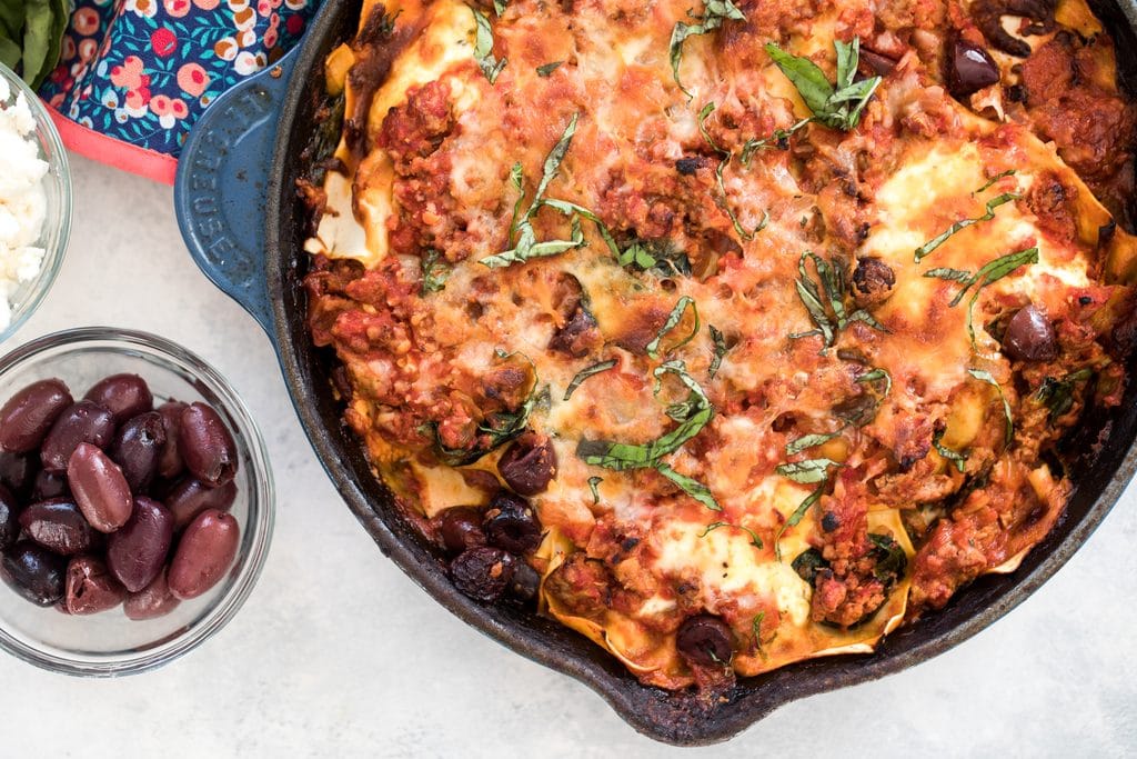 Landscape view of Greek lasagna in a skillet with kalamata olives in a small bowl to the side