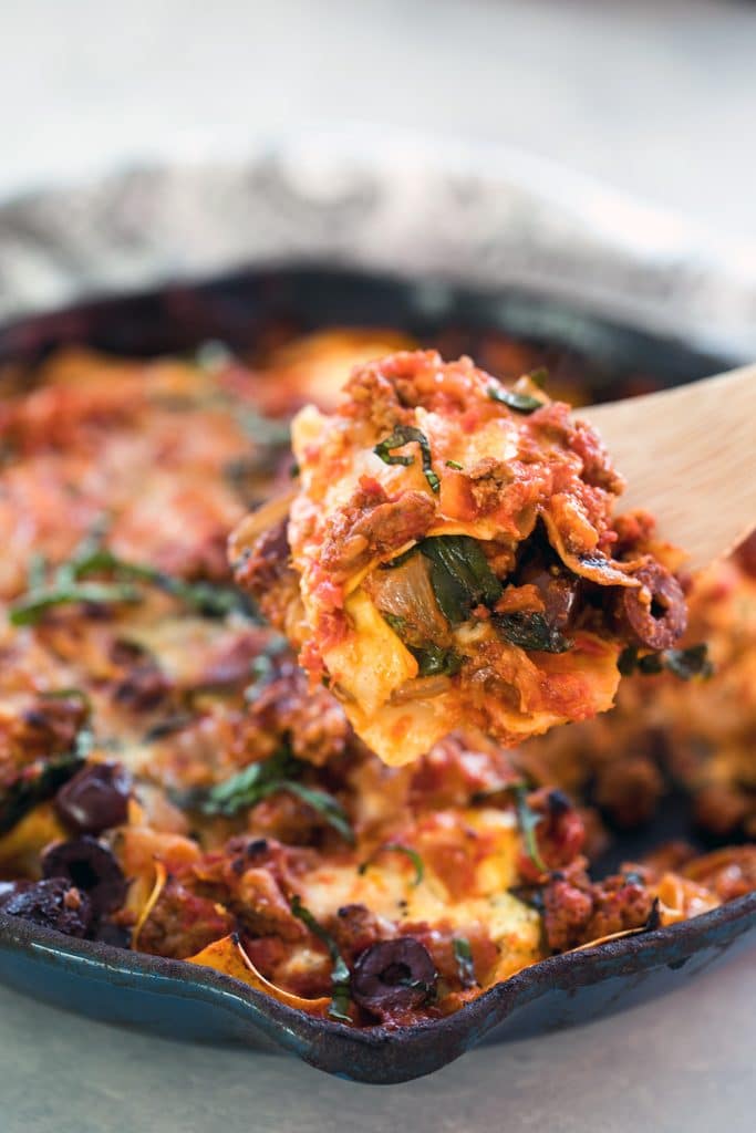 Head-on view of a spoon taking a scoop out of greek lasagna in skillet