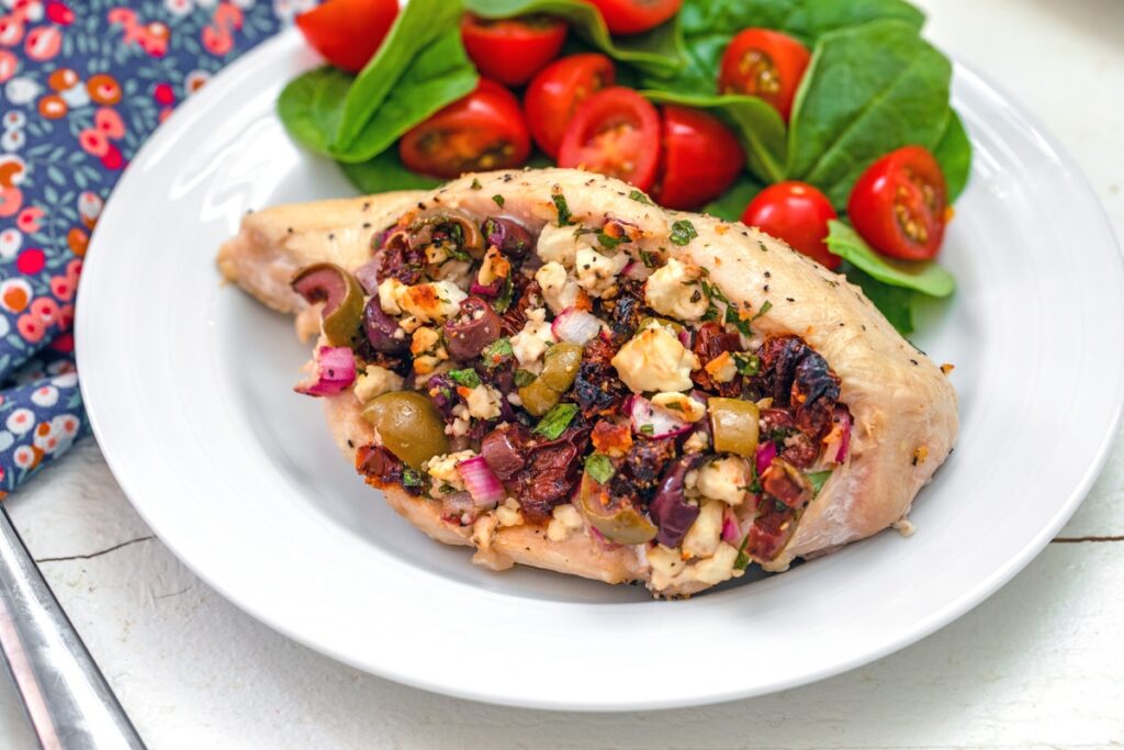 Horizontal head-on view of a Greek-stuffed chicken breast with spinach salad on side
