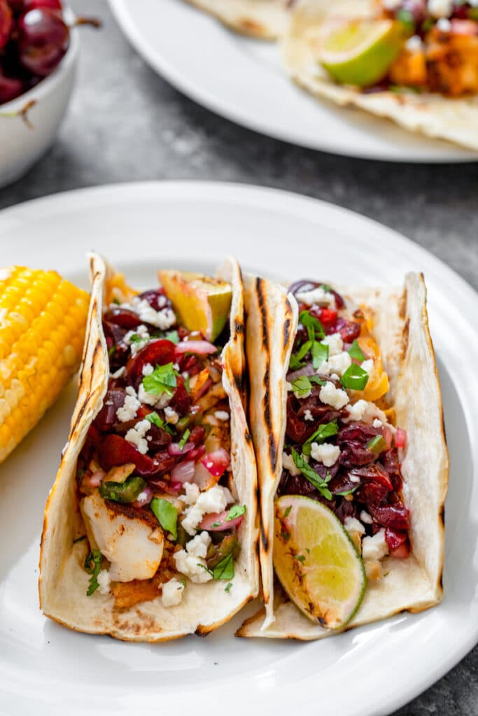 Head-on view of two grilled cod tacos with grilled cherry salsa