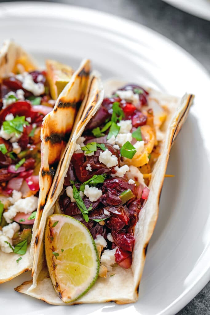 Overhead closeup view of grilled cod tacos with cherry salsa, cheese, scallions, onions, and lime