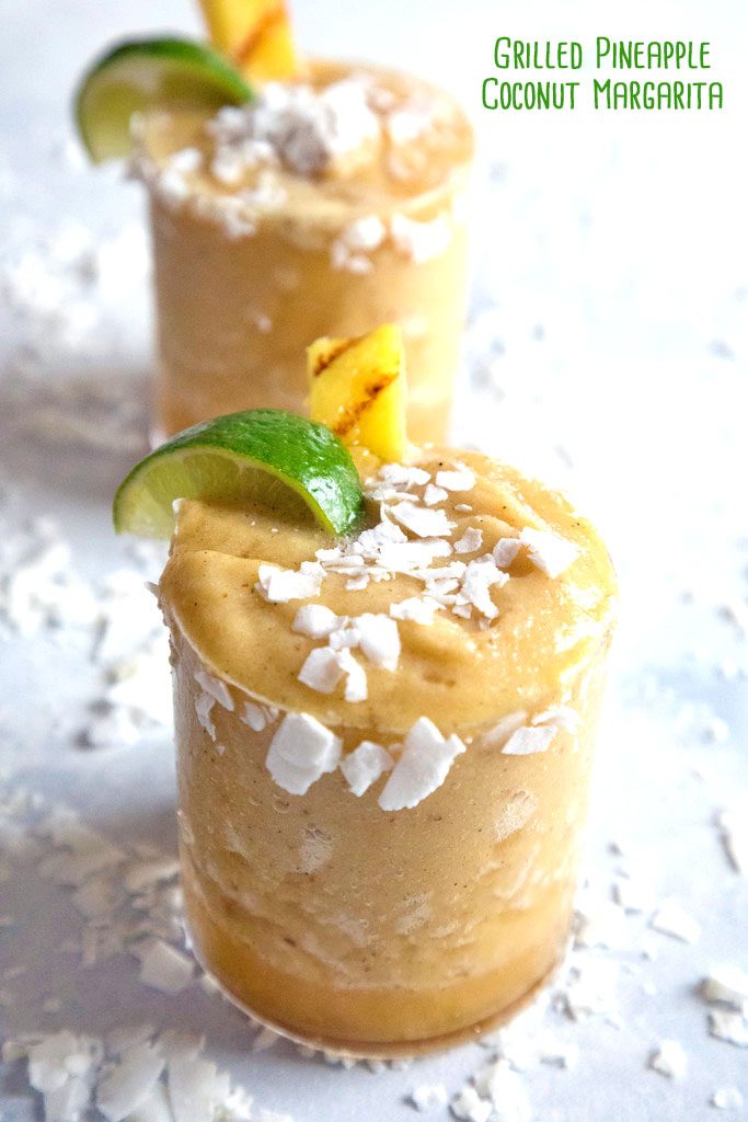 Head-on view of grilled pineapple coconut margarita with coconut, lime, and pineapple garnish with second cocktail in background and recipe title at top