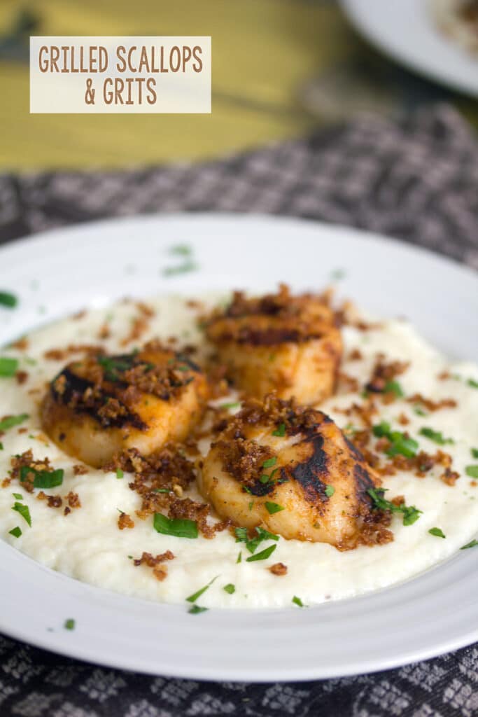 Head-on view of a plate with cheesy grits and grilled scallops with recipe title at top