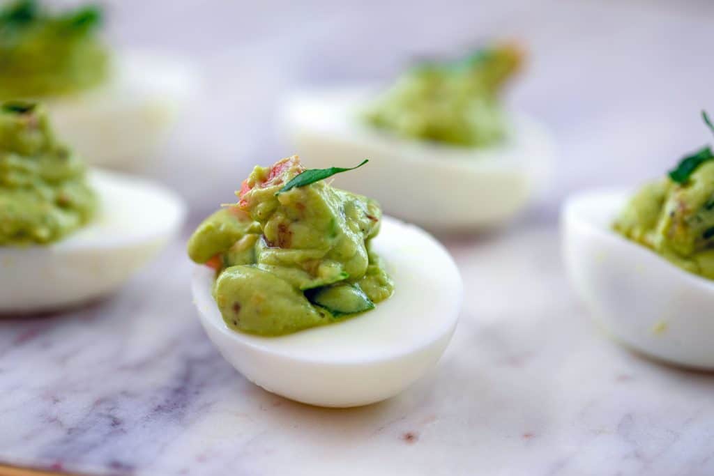 Landscape photo head-on close-up of guacamole deviled egg on marble surface with additional eggs around