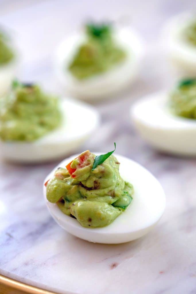 Head-on view of guacamole deviled egg on marble surface with other eggs in the background