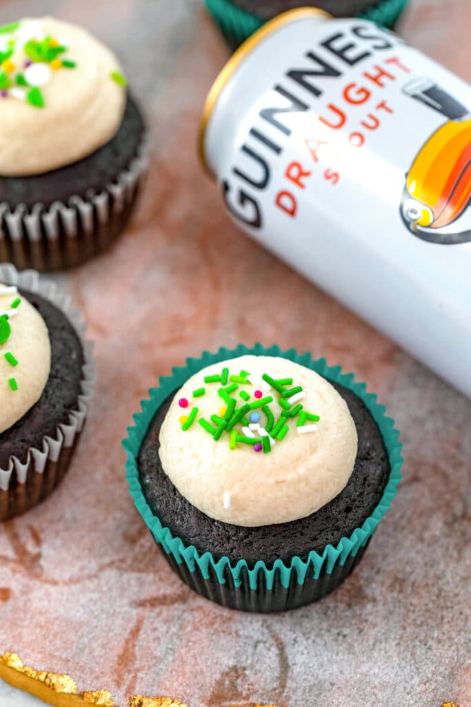 Overhead view of a Guinness cupcake with buttercream and green sprinkles with more cupcakes and can of Guinness in background