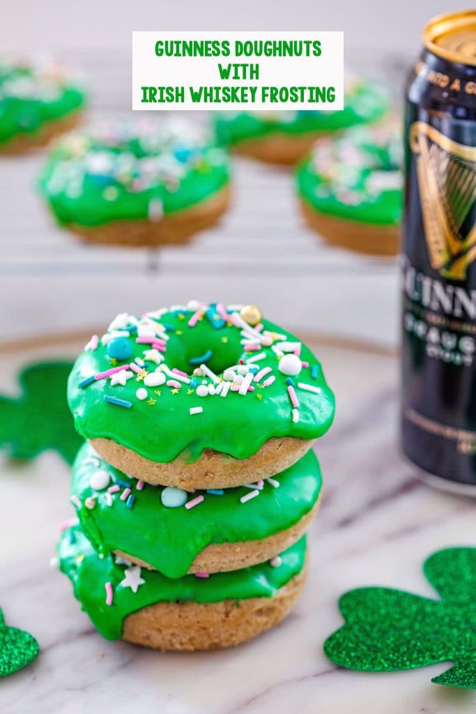 Stack of four Guinness doughnuts with baking rack with more doughnuts in the background, a tall can of Guinness beer, glitter shamrocks, and the recipe title at the top of the image