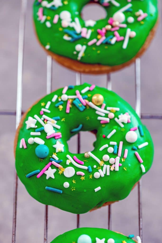 Overhead view of bright green Guinness doughnuts with colorful sprinkles on a baking rack