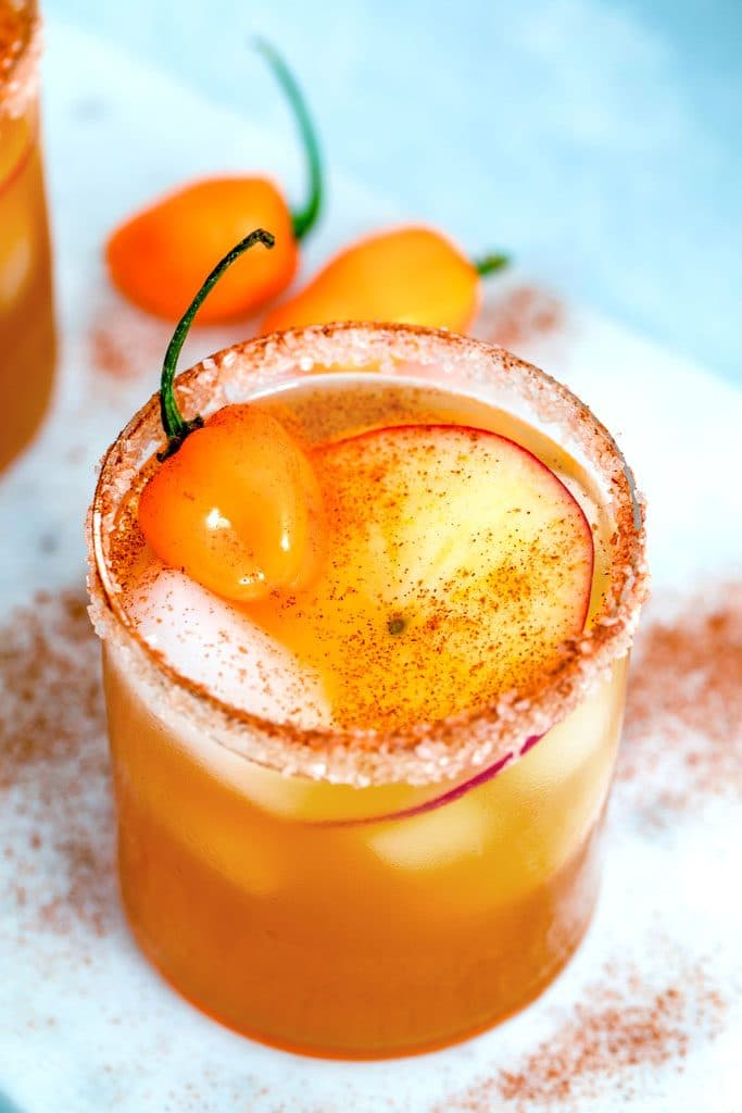 Overhead view of habanero ginger apple cider cocktail with apple and habanero pepper garnish on a marble board sprinkled with cinnamon and habanero peppers