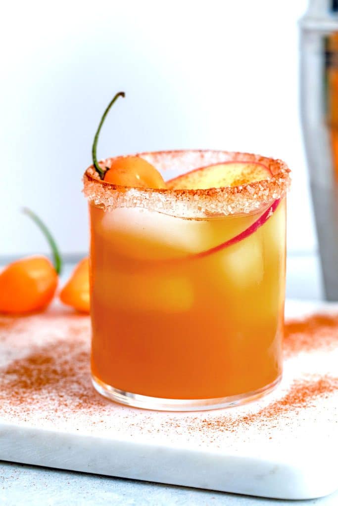 Head-on image of habanero ginger apple cider cocktail with apple and habanero garnish on marble board sprinkled with cinnamon