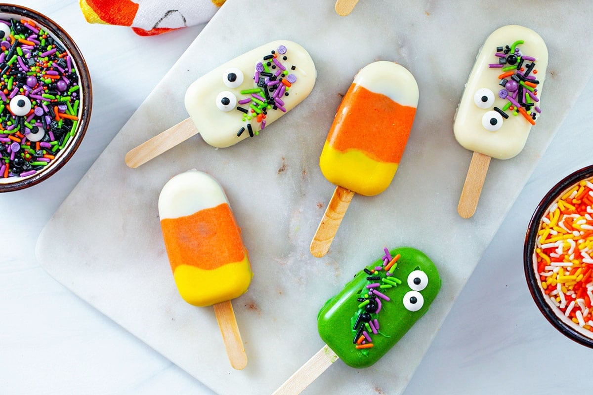 Landscape overhead view of Halloween cakesicles on a marble slab with Halloween sprinkles in background.