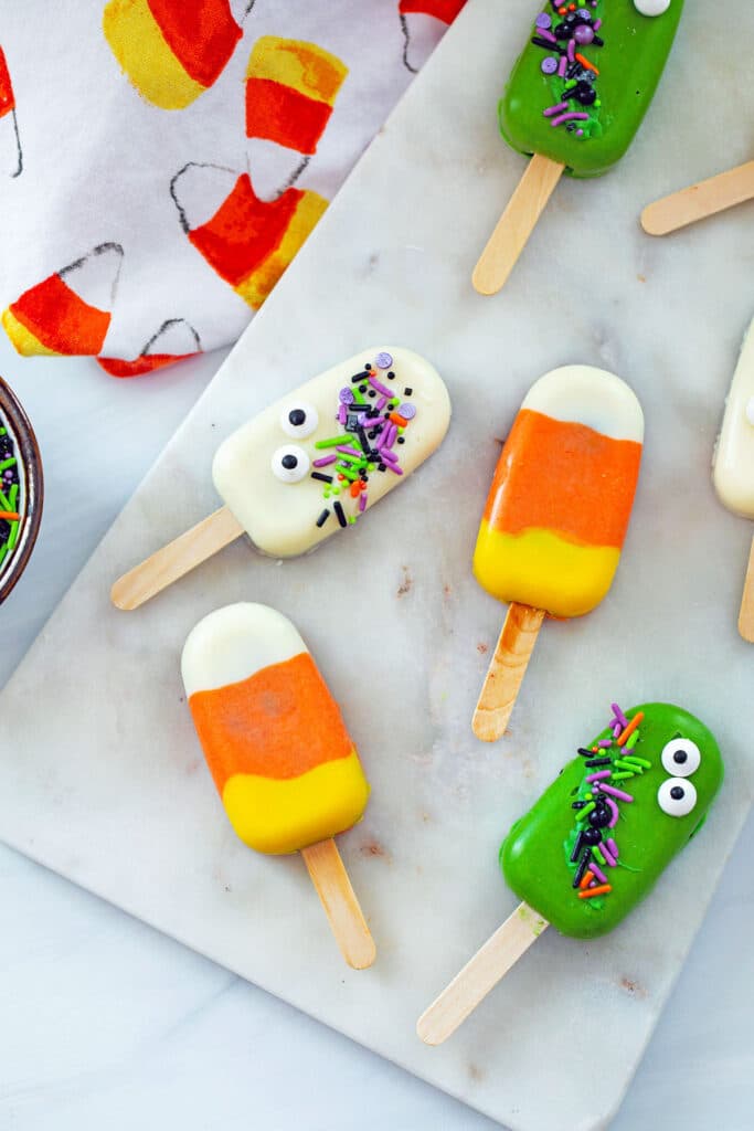 Overhead view of various Halloween Cakesicles on marble board, including candy corn cakesicles and ghost cakesicle