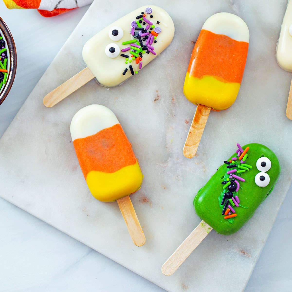 Overhead closeup view of various Halloween Cakesicles on marble board, including candy corn cakesicles and ghost cakesicle