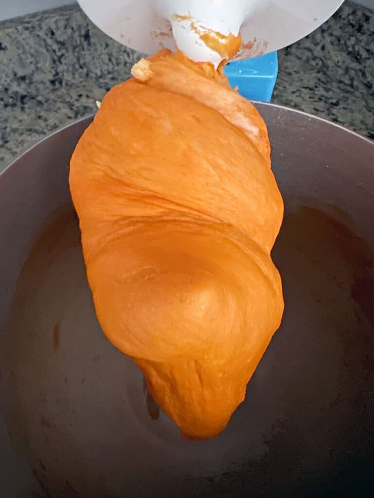 Orange cinnamon roll dough being kneaded on the dough hook of a mixer.