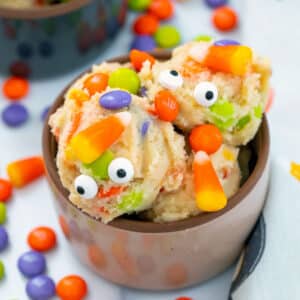 Closeup view of Halloween cookie dough in a small bowl and topped with candy corn, M&Ms, and googly eyes.