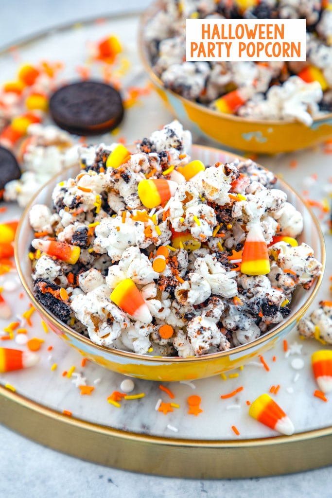 Overhead view of a bowl of Halloween party popcorn with candy corn, orange and yellow sprinkles, and Halloween Oreo cookies all around and a second bowl of popcorn in the background with recipe title at top
