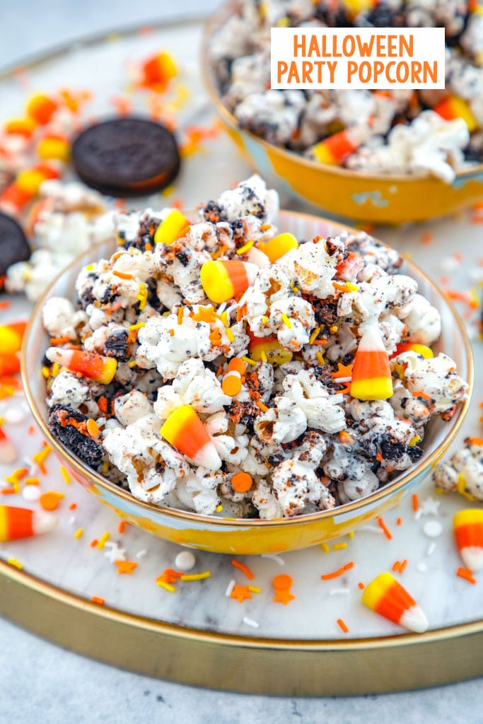 Overhead view of a bowl of Halloween party popcorn with candy corn, orange and yellow sprinkles, and Halloween Oreo cookies all around and a second bowl of popcorn in the background with recipe title at top.