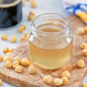 Closeup view of a small jar of hazelnut syrup with whole hazelnuts all around.