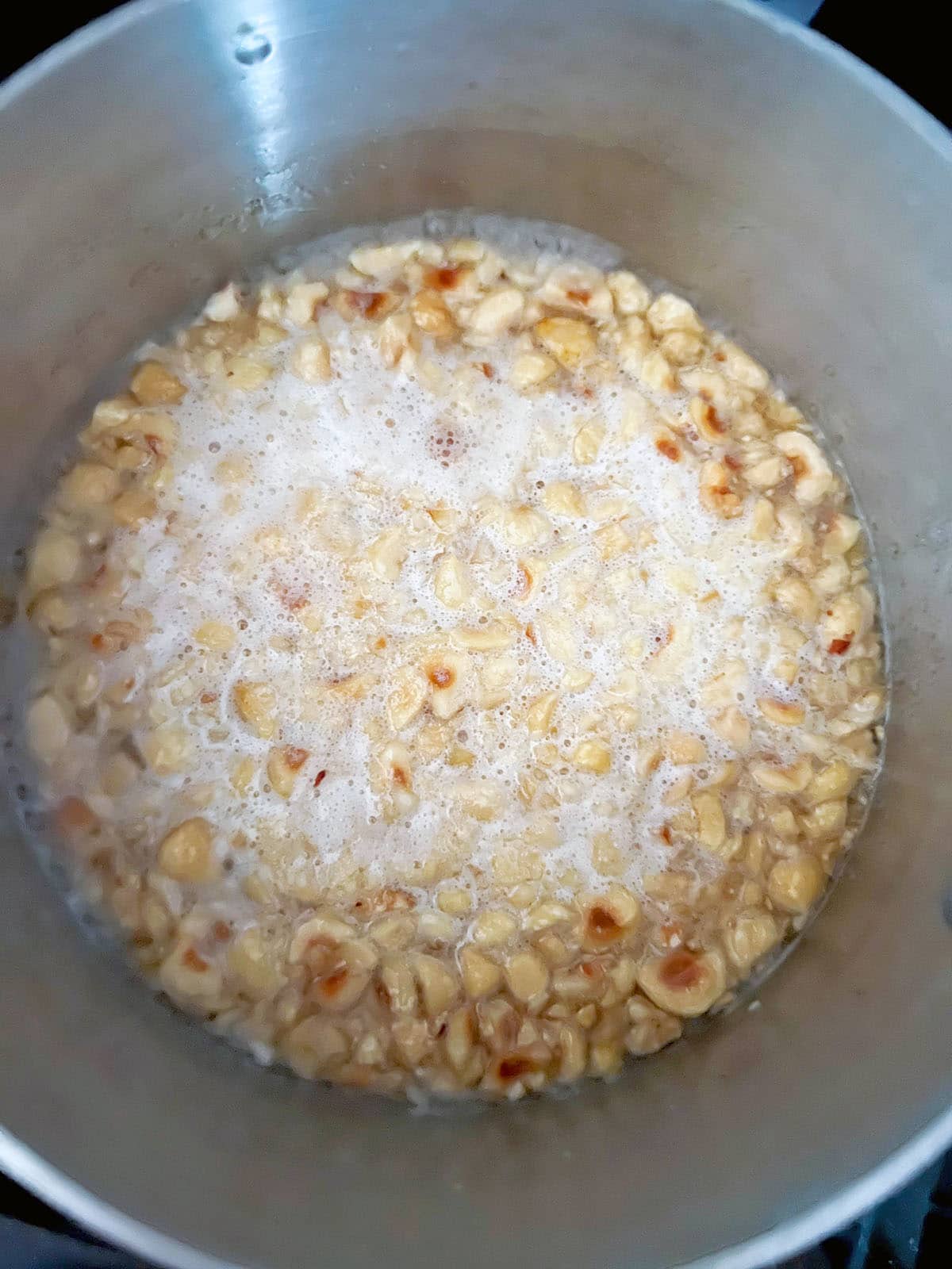 Hazelnuts boiling in sugar water in saucepan.