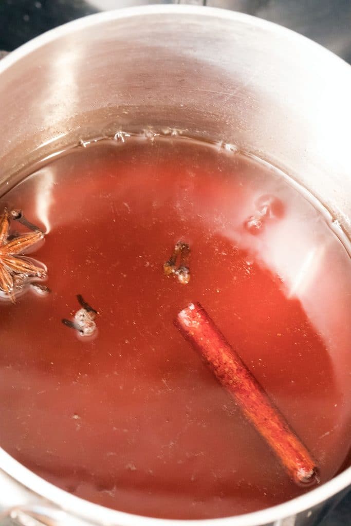 Overhead view of holiday spiced simple syrup in a saucepan with cinnamon stick, star anise, and cloves