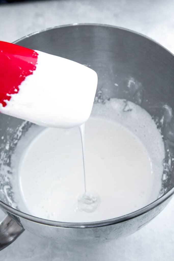 Homemade marshmallow fluff dripping off spatula in mixing bowl.