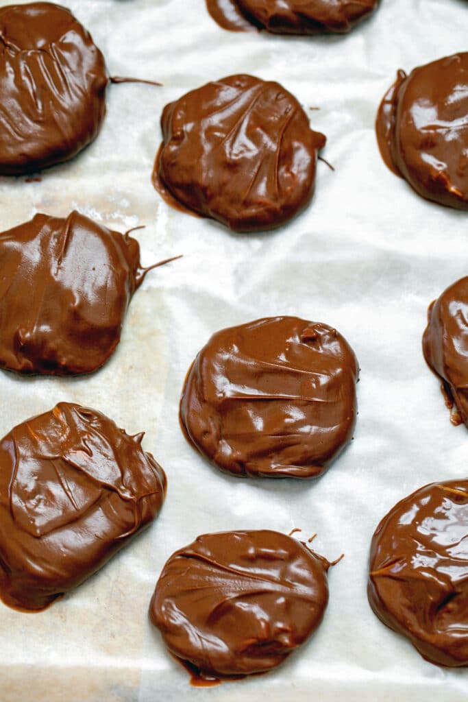 Tagalong cookies just dunked in chocolate resting on waxed paper.