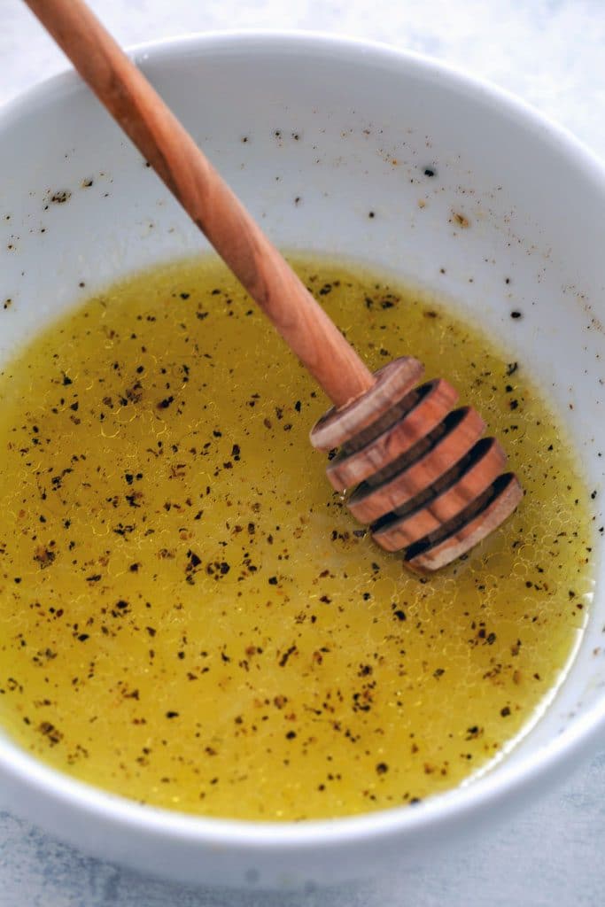Bowl of honey lime dressing with honey stick and black pepper