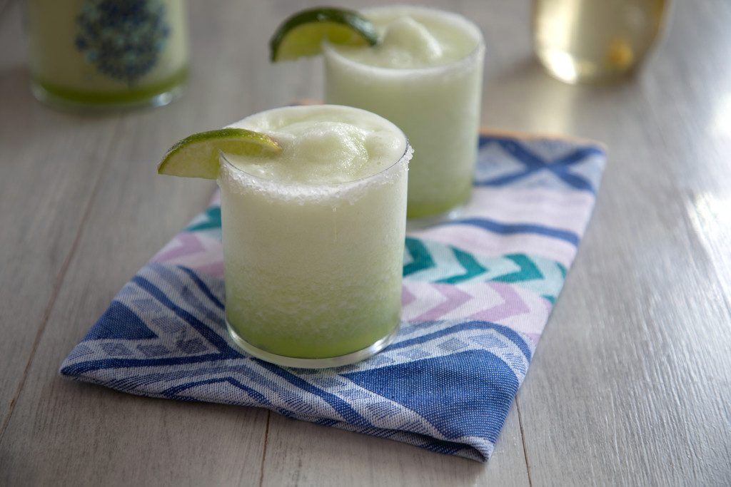 Landscape head-on view of two honeydew margaritas with lime wedge garnishes on a colorful napkin
