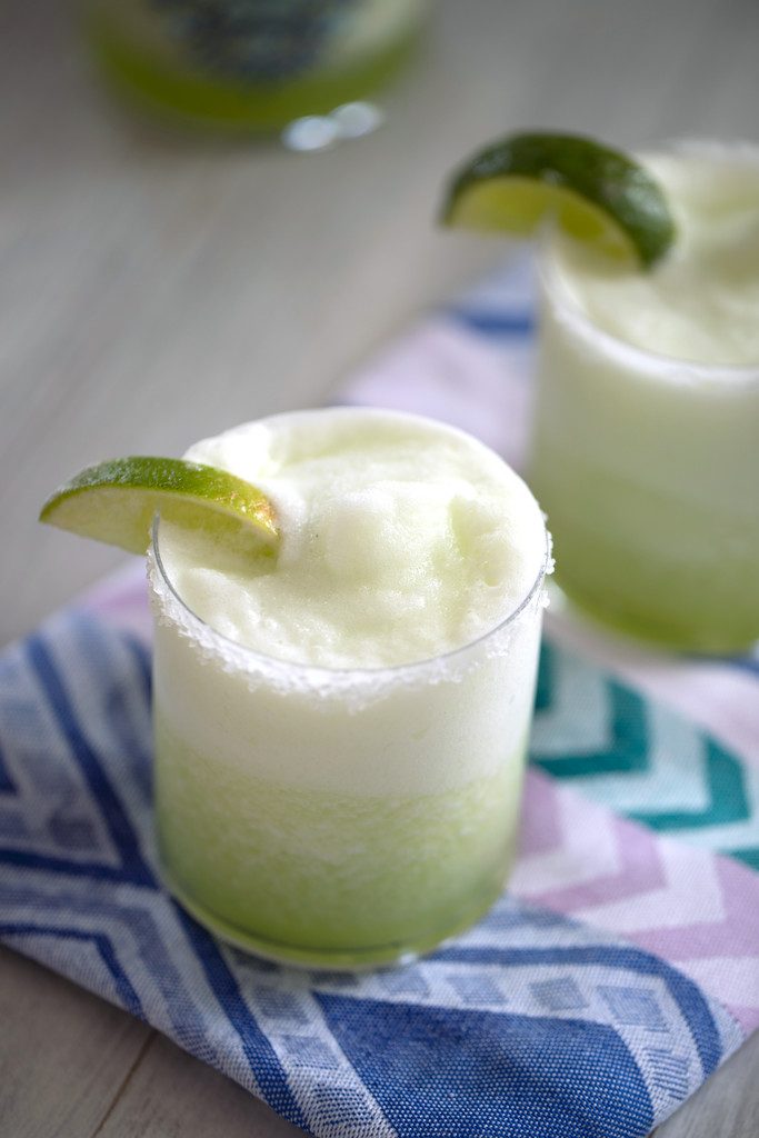 Close-up overhead view of a honeydew margarita with lime wedge garnish on a colorful napkin with second margarita in the background