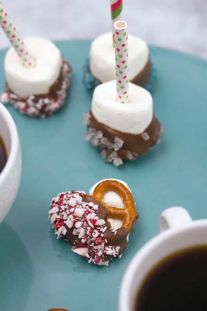 Overhead view of a hot chocolate peppermint pretzel bite surrounded by chocolate-dipped marshmallows and mugs of coffee