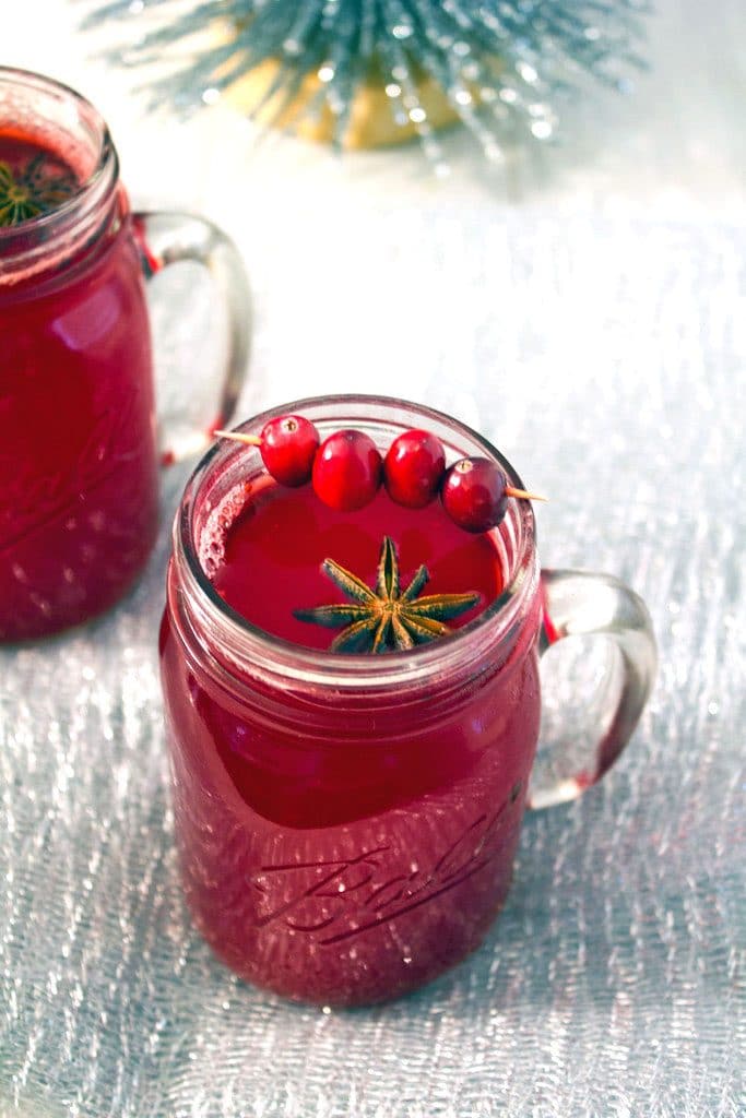 Overhead view of a mason jar filled with hot spiced cranberry cocktail with star anise and cranberry garnish and a second cocktail in the background