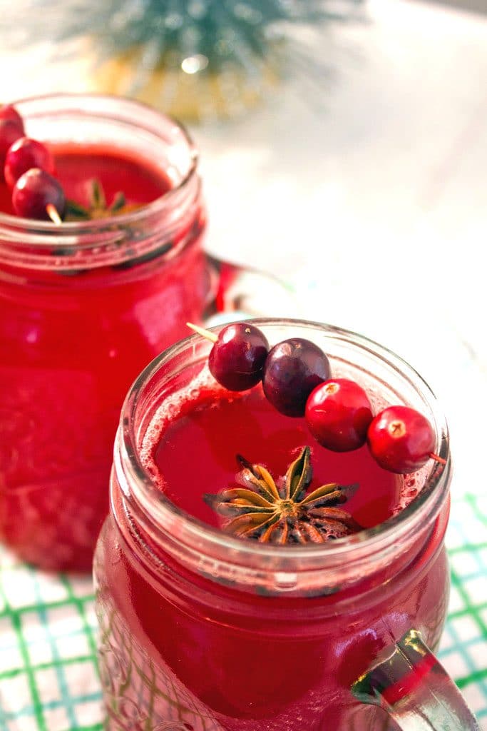 Overhead view featuring the top of a mason jar filled with hot spiced cranberry cocktail with star anise and cranberry garnish and a second cocktail in the background