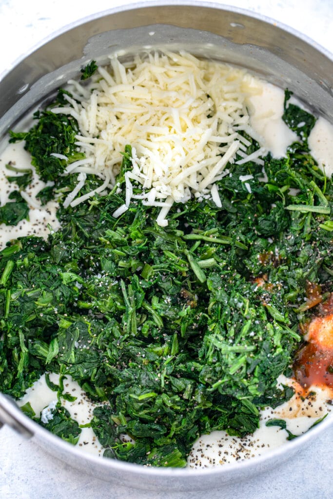 Overhead view of spinach, shredded cheese, and hot sauce in saucepan with milk and cream cheese