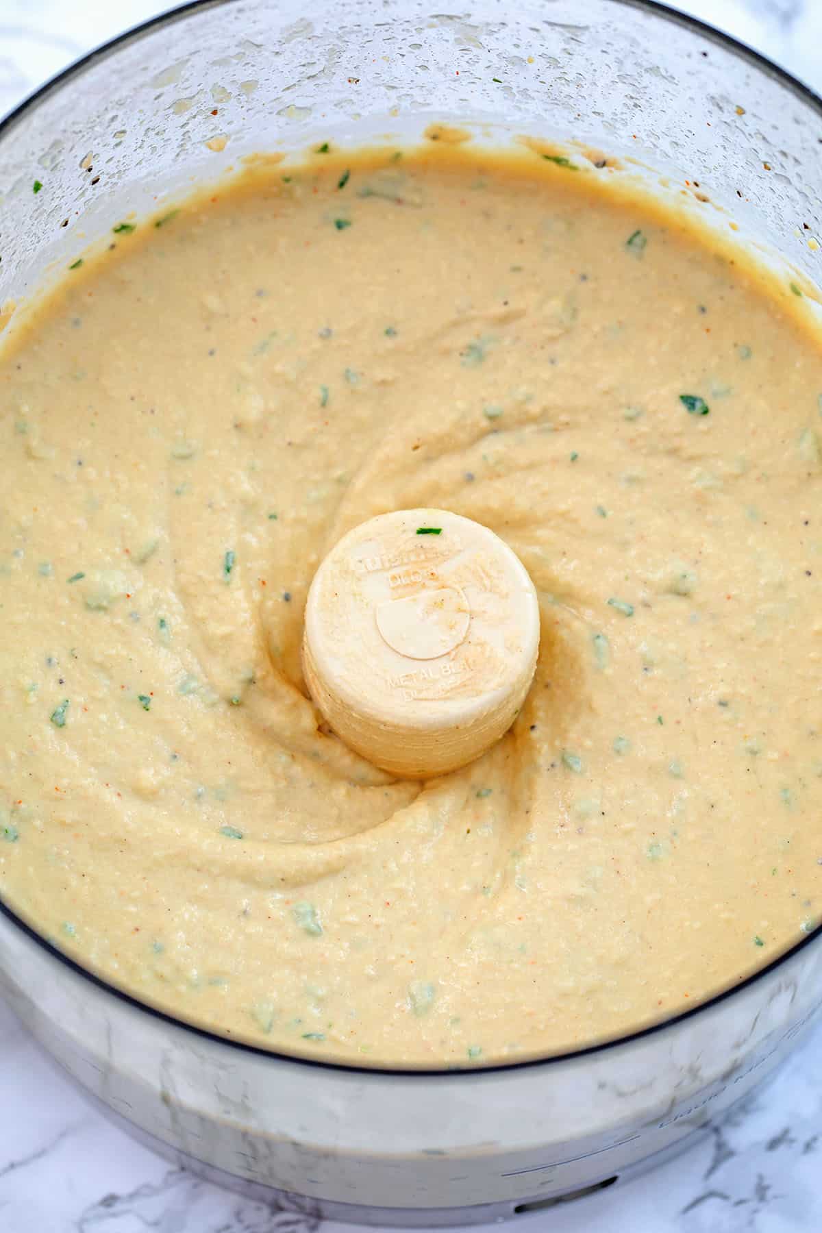 Hummus with parsley in food processor bowl.