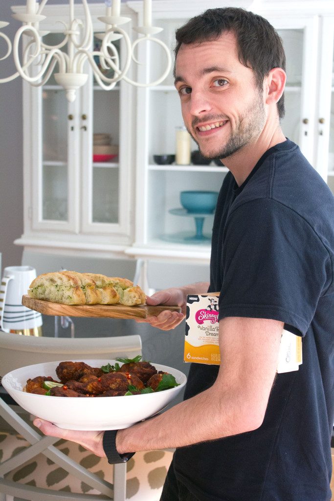 Chris holding bowl of spicy Thai chicken drumsticks, garlic bread, and ice cream sandwiches, looking sneaky