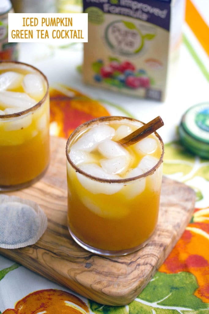 Overhead view of a glass of iced pumpkin green tea cocktail with a cinnamon rim and cinnamon stick on a wooden board with second cocktail and tea bags in background with recipe title at top