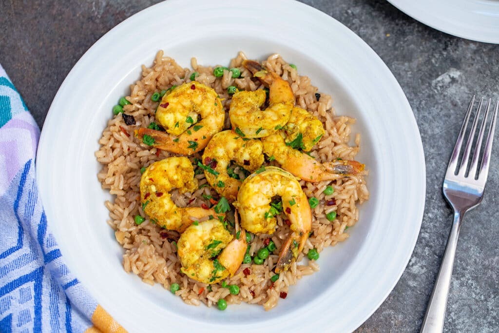 Landscape overhead closeup view of a white bowl with brown rice with peas topped with Indian style shrimp