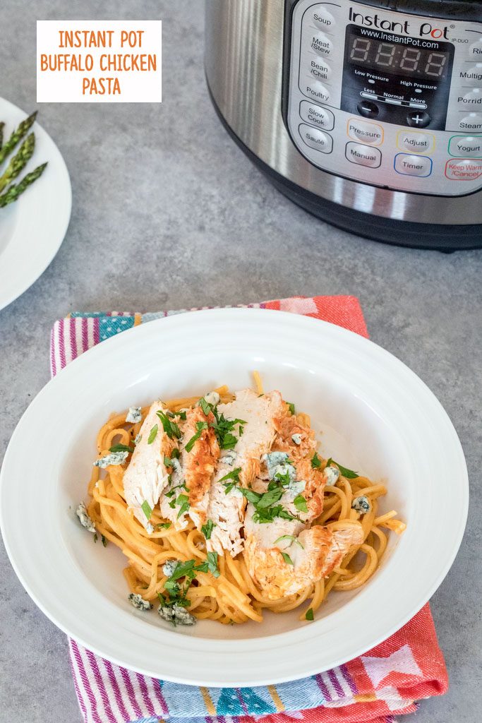 Overhead view of buffalo chicken pasta in white bowl with bowl of asparagus and Instant Pot in the background and recipe title at top