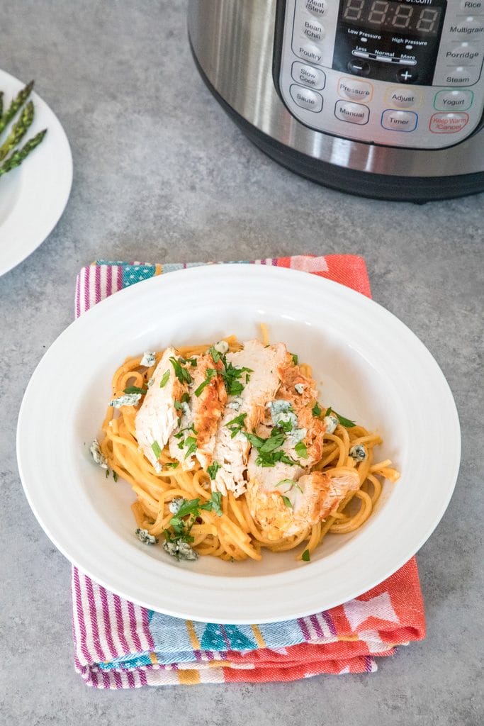 Overhead view of buffalo chicken pasta in white bowl with bowl of asparagus and Instant Pot in the background