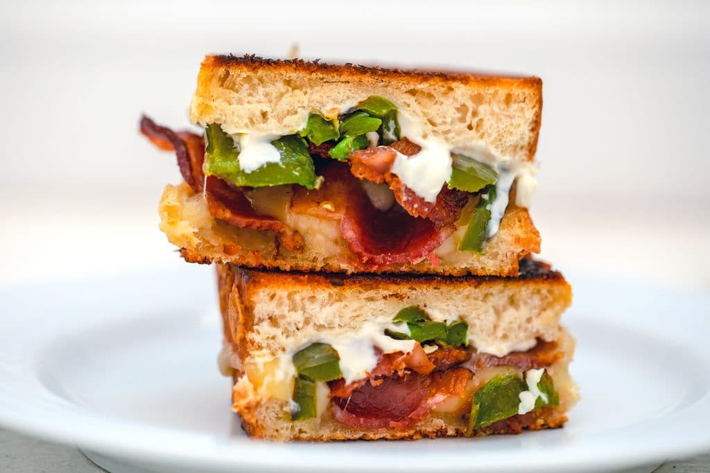 Landscape view of two halves of jalapeño popper grilled cheese stacked on each other on a white plate