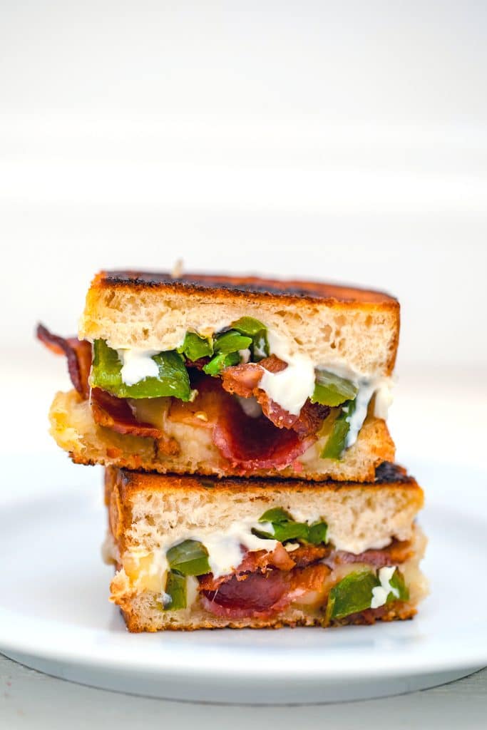 Head-on view of two halves of a jalapeño popper grilled cheese sandwich stacked on top of each other on a white plate