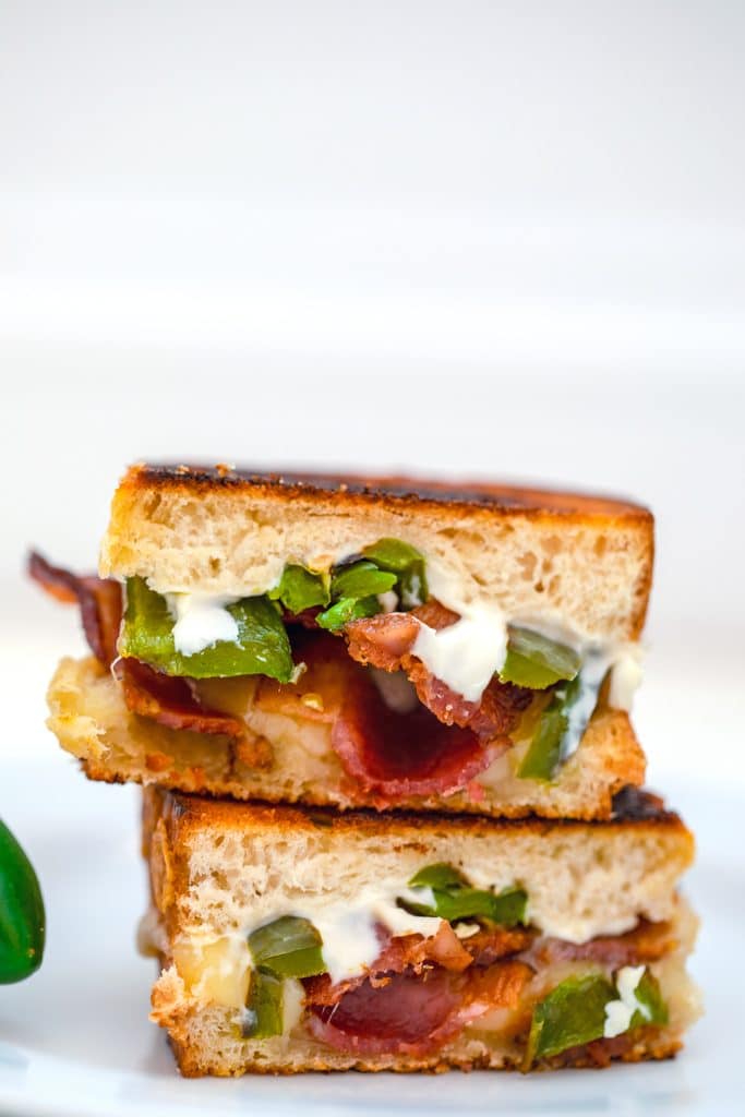 Close-up head-on photo of two jalapeño popper grilled cheese sandwich halves stacked on top of each other on a white plate