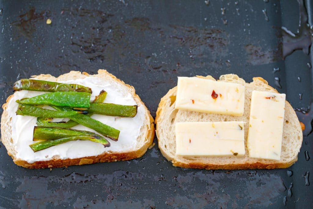 Two slices of bread on griddle, one with cream cheese and jalapeño slices and one with sliced pepper jack cheese