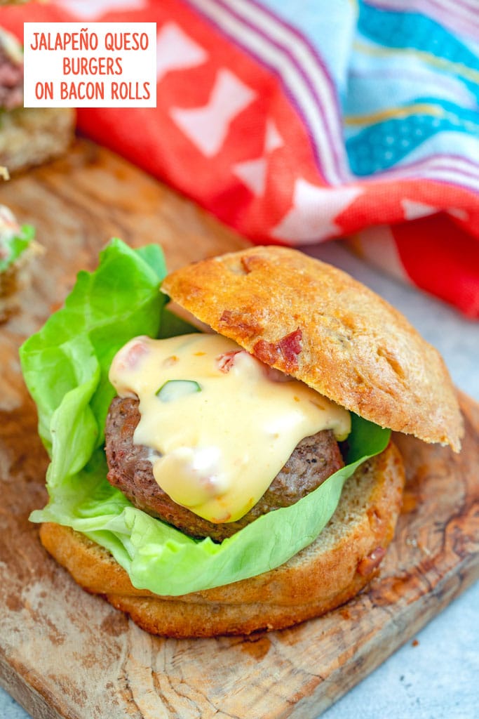 Overhead closeup view of a jalapeño burger with lots of queso on a bacon roll with a leaf of lettuce on a wooden cutting board with recipe title at top