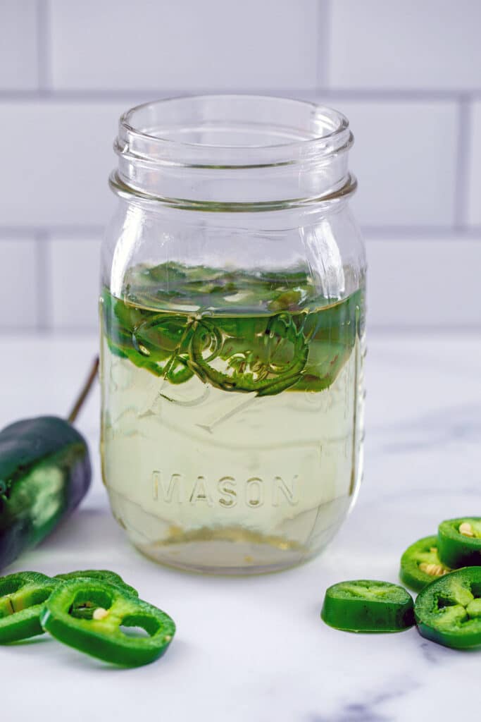 Head-on view of a mason jar filled with jalapeño simple syrup with sliced peppers in the syrup and all around jar