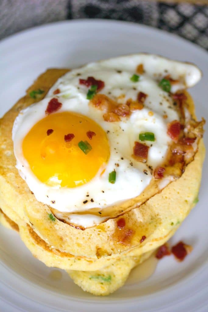 An up-close view of a stack of jalapeño bacon corn pancakes with a sunnyside up egg on top and crumbled bacon and chives