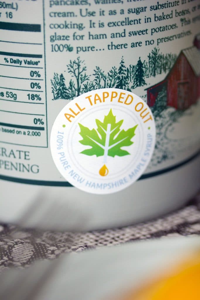 An up-close view of a bottle of maple syrup with "All Tapped Out" sticker