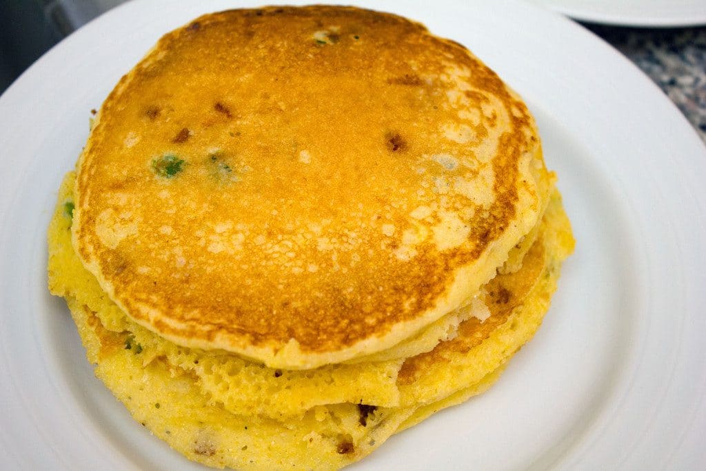 A stack of golden jalapeño bacon corn pancakes on a white plate