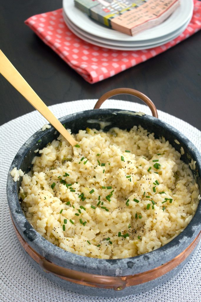 Overhead view of large soapstone serving dish of jalapeño risotto with chives on top and gold serving spoon