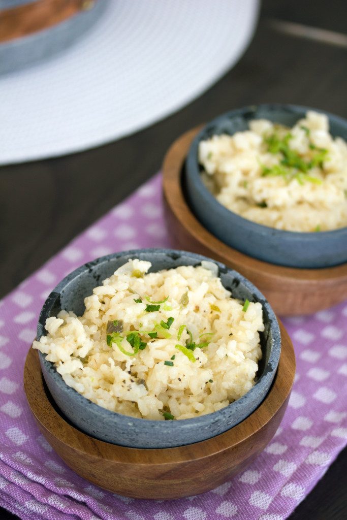 Overhead closeup view of two soapstone bowls of jalapeño cheddar risotto with chopped chives on a purple placemat